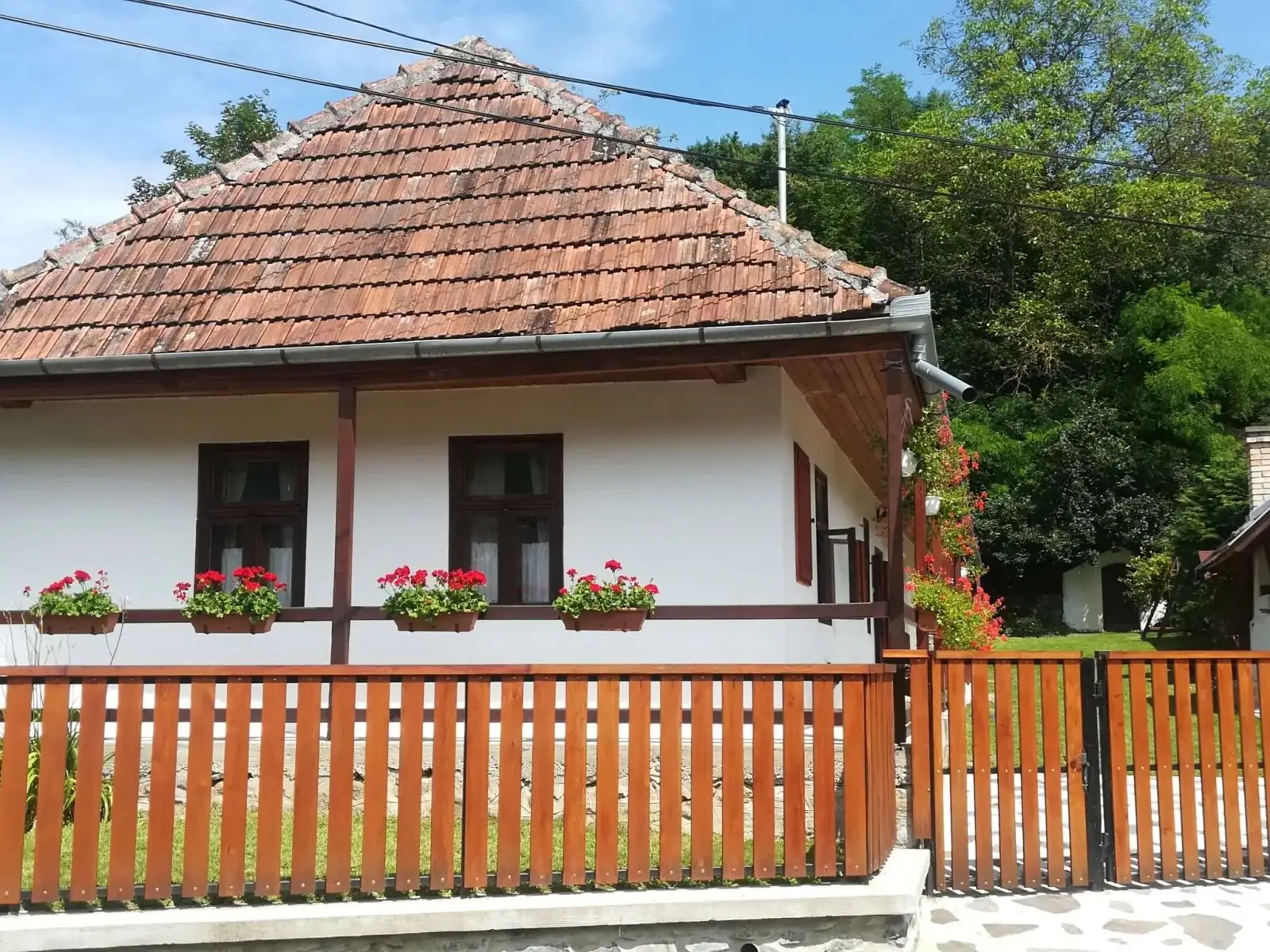 A Barát-bérc Vendégház fehér falú, cseréptetős parasztháza muskátlis ablakokkal és faléces kerítéssel